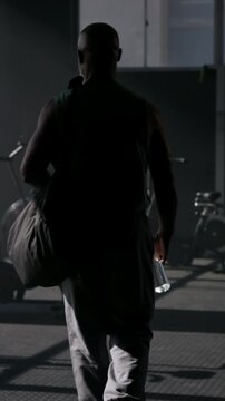 Athlete, man and walk in gym with bag for spin class arrival, fitness preparation or drinking water. Back, mature black person and reflection at health club for bike exercise, getting ready or window