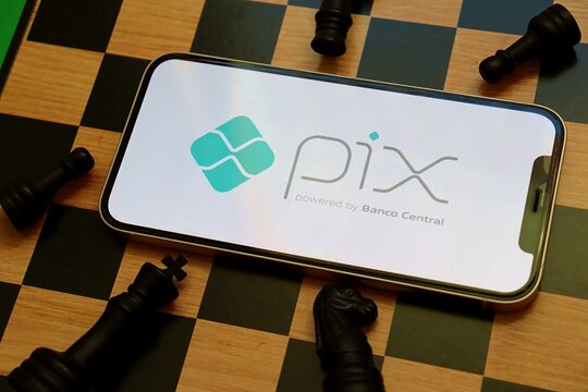 S&atilde;o Paulo, Brazil - April 29, 2026: Pix payment system logo on a smartphone screen placed on a chessboard. Financial strategy concept. Pix Banco Central.