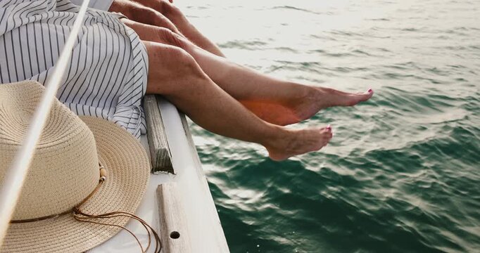 Couple's legs dangling off the side of a boat while sailing on the sea during a summer vacation