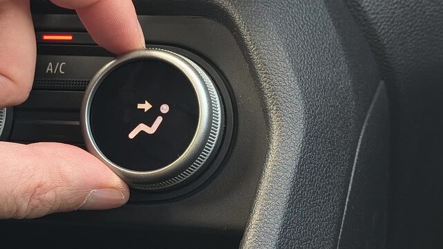 Close up of hand adjusting car climate control airflow direction knob, selecting air to feet mode, modern vehicle interior dashboard, ventilation system operation detail