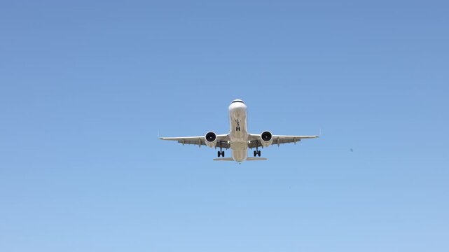 A passenger airplane flying in a clear blue sky. View of the airplane from below showing its underside.
