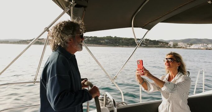 Happy senior couple enjoying a vacation, with the woman taking selfies while the man steers the boat