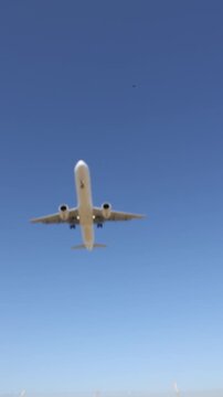 A passenger airplane flying in a clear blue sky. View of the airplane from below showing its underside.