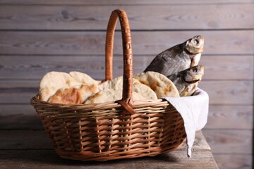 Obraz premium Fresh loaves of bread and dried fish in wicker basket on wooden table, closeup