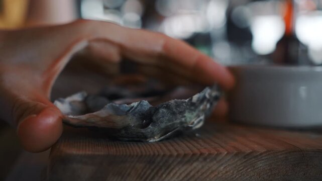 Hands reach for an oyster on a wooden table in a busy restaurant during early evening hours