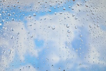 Obraz premium Window with water drops. View on blue sky with clouds through wet glass