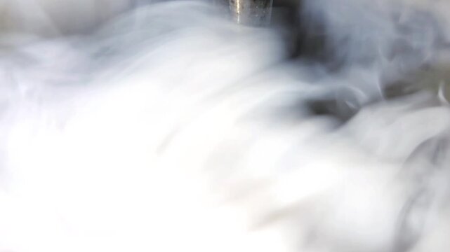 Thick white smoke or vapor swirling around a metal pipe in an industrial machine. Industrial smoke generator closeup.
