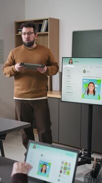 Vertical shot of male teacher leading computer class for adults and giving lecture while standing by digital screen with social media page example