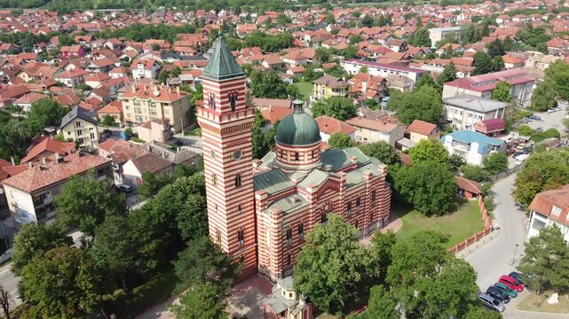 A cinematic aerial drone flight moving forward towards the Church of the Holy Trinity in Paracin, Central Serbia. The shot is framed to focus on the dominant church tower and a sea of orange rooftops.