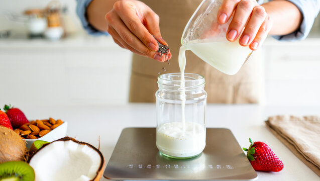 Hands pouring milk into a jar on a digital scale in a kitchen, ingredient measurement, healthy food prep, portion control, home cooking.