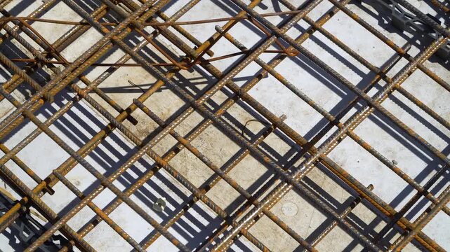 Rusty rebar mesh on concrete slab before pouring, sunny day.