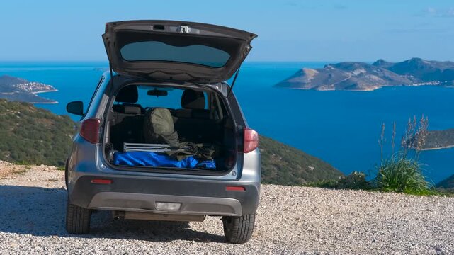 Car parked on coastal mountain road for adventurous travel. Suv with open trunk packed with camping gear parked at a scenic coastal viewpoint overlooking sea and islands, ready for hiking, trekking