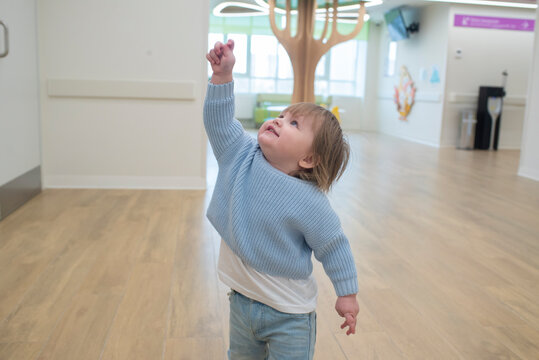 Cute toddler boy pointing up and looking up in modern polyclinic hall