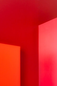 Three intersecting walls with copy space in shades of red and orange form sharp geometric angles. The surfaces provide a smooth background, evenly lit, with no visible details or textures.