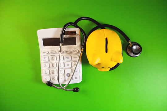 Piggy bank with stethoscope and calculator on green background