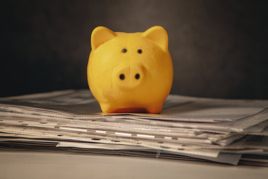 Piggy bank on top of a pile of newspapers on a dark background