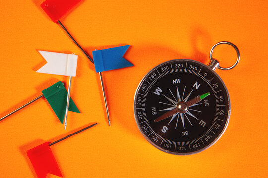 Compass, pins and flags on an orange background. Top view