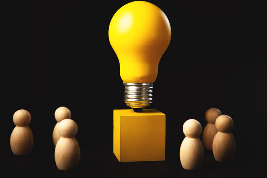 Light bulb and wooden figures on black background. Business idea concept.