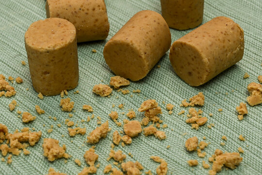 Traditional Brazilian peanut candy known as pacoca de rolha, featuring cylindrical shapes and crumbs scattered on a green textured fabric background, perfect for dessert or festive celebrations