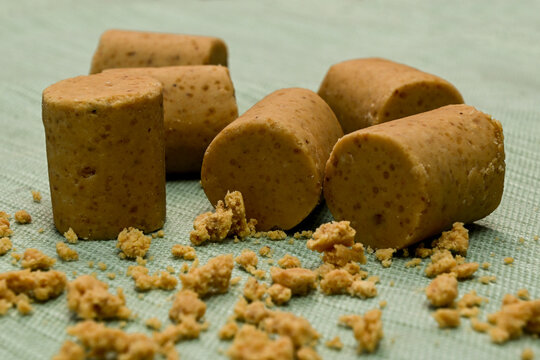 Traditional Brazilian peanut candy known as pacoca de amendoim in a cylindrical shape, scattered with crumbs on a green textured background, perfect for dessert or Festa Junina celebrations