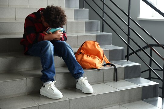 Bullying. Upset boy with backpack on stairs at school