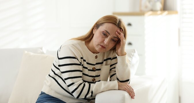 Menopause. Woman suffering from headache on sofa at home