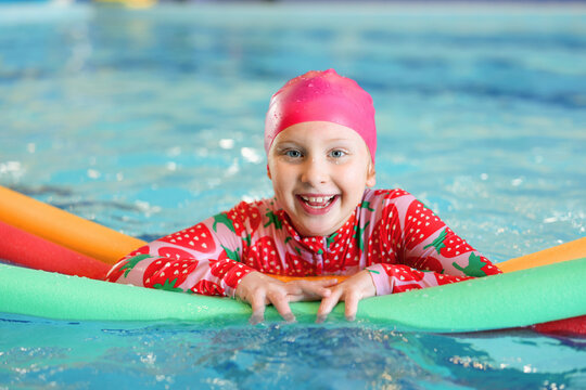 Cute little girl swimming with water noodles during lesson in pool