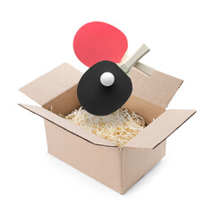 Ping pong rackets and ball falling into cardboard box with shredded paper filler on white background