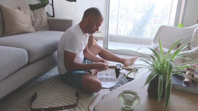 Man assembling a baby bouncer chair on the floor following the instruction manual at home