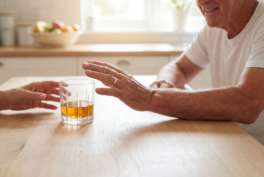Older man pushing away a glass of alcohol on a kitchen table