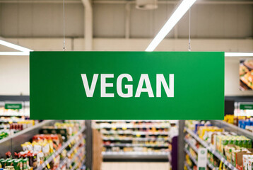 Obraz premium Green VEGAN sign hangs in supermarket aisle for healthy food