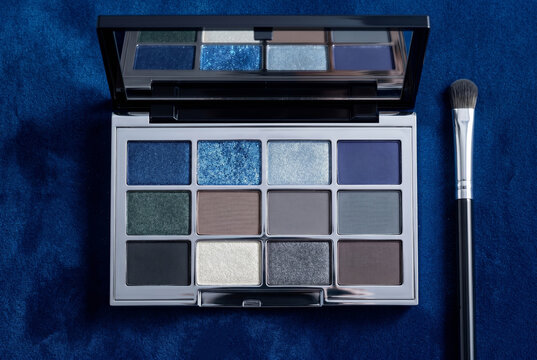 Top view of an open eyeshadow palette with shimmering blue, silver, and dark grey shades
