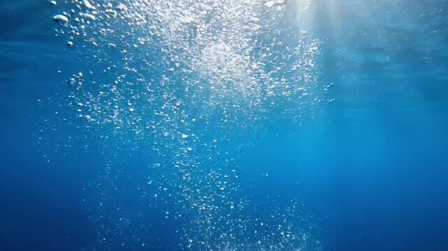 Blue water with bubbles moving in slow motion under bright light at deeper depth in the ocean