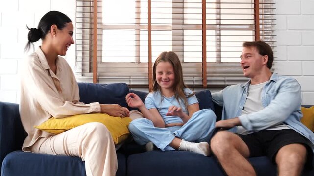 A warm and happy family is in the living room at home: father, mother, and their nine-year-old daughter sit on a couch. The father tells stories and sings songs with his daughter, while the mother hol