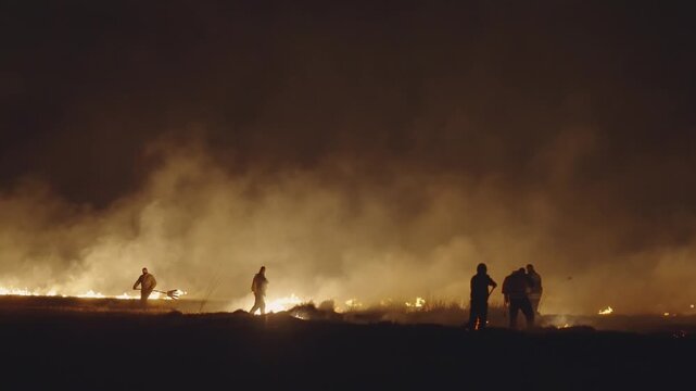 Silhouette team of firefighters estinguishing fire at night, slow motion