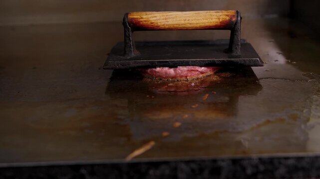 searing a fresh burger patty with a heavy cast iron grill press