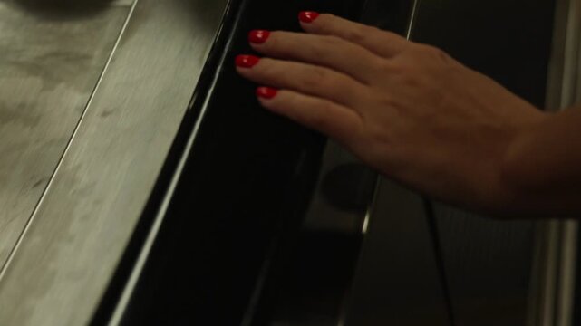 Close up female hand with red manicure holding escalator handrail moving upward in modern shopping mall transportation lifestyle video footage