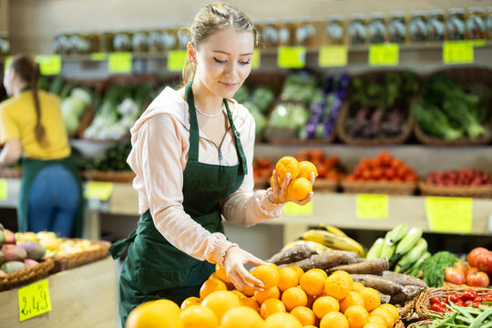 Girl employees in uniform holding fresh mandarines in grocery shop