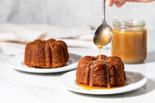 Freshly baked sticky toffee pudding with a spoon dripping caramel sauce on top.
