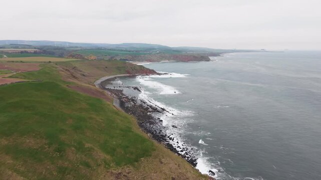 Cinematic aerial fly forward over high coastal cliffs and green hills toward the misty horizon, Scotland.