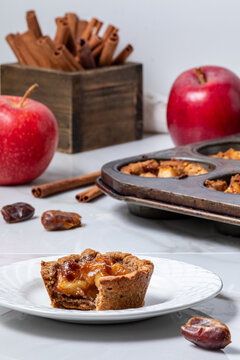 A mini apple pie tart with a muffin tin of the rest and ingredients all around.