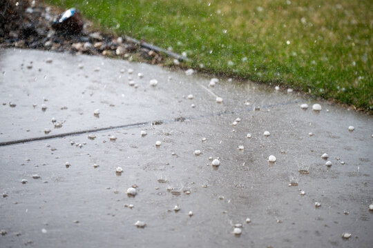 Heavy rain falls and hail accumulates on the sidewalk in a residential area during the afternoon
