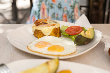 Beautiful woman eating a traditional breakfast featuring avocado eggs green plantain and fresh tomato salad. © Alejandro