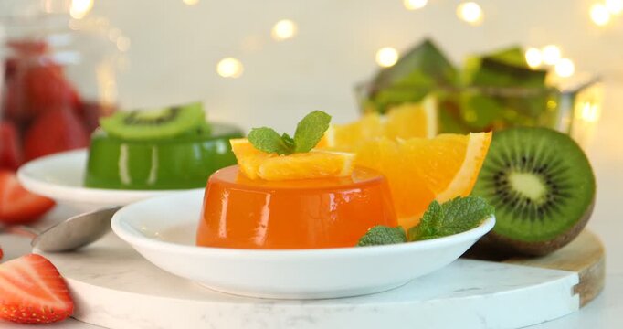 Woman putting mint on tasty jelly with orange slices at table, closeup
