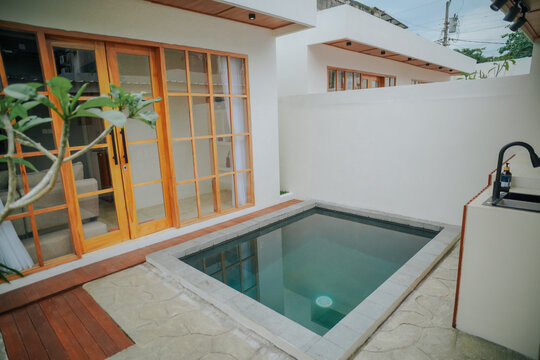 A small private swimming pool is located in the outdoor area of ​​a modern minimalist residence with a dominant white color and wooden accents.