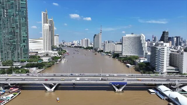 Vehicles moving across King Taksin Bridge and boats on river below. Traffic and water transport movement across city.