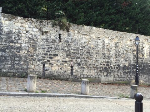 A rustic ancient stone wall bordering a cobblestone street in a quiet Parisian neighborhood.