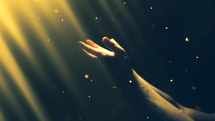Naklejka premium A man's hand reaches out to the shimmering divine rays of bright golden light in the darkness. The concept of religion, God, soul, faith.