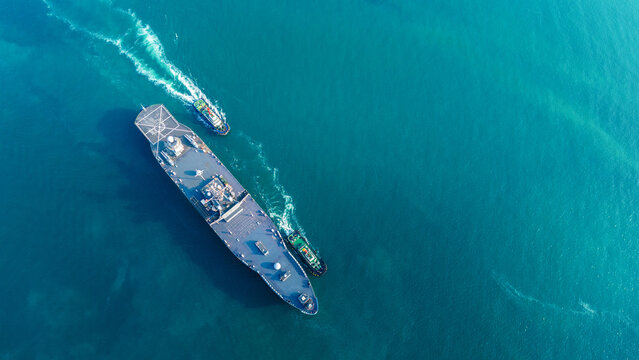 large naval amphibious assault ship being assisted by tugboats in the strategic Strait of Hormuz. Concept of maritime security, naval power projection, and protection of international shipping lanes.
