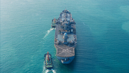 stern view of a naval warship being assisted by tugboats in the strategic Strait of Hormuz. Concept of maritime security, naval defense operations, and geopolitical tension in international waterways. © Yellow Boat